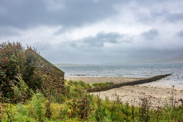 Sandstrand mit altem Steinhaus am Evie Pier in Schottland
