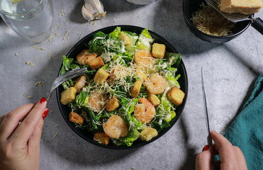 close up of woman eating Cesar salad with fork on grey marble table