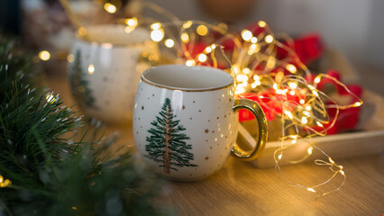 Two New Year's cups on the background of New Year's lights. Cups with New Year's print in the form of a Christmas tree. Decor for a New Year's feast