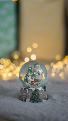Christmas ball with snow on the background of Christmas lights. New Year's Santa Claus in a ball with snow on a warm carpet.
