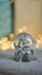 Christmas ball with snow on the background of Christmas lights. New Year's Santa Claus in a ball with snow on a warm carpet.