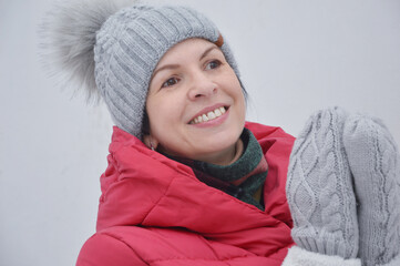 Portrait of a smiling young woman in a knitted gray hat and mittens. A woman in a red hooded jacket looks into the distance.