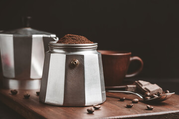 Moka coffee pot filled with brown ground coffee on dark wooden board, prepare to brewing Italian espresso