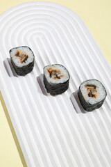 Asian culture, Japanese hosomaki (sushi, rolls) with eel on yellow background. Oriental culinary, eastern cooking.