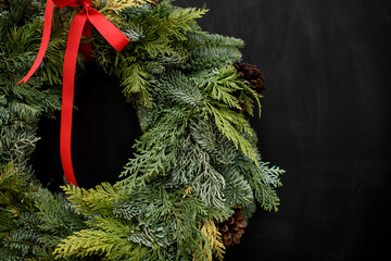 Close-up of wreath made of fir branches, tuja, spruce with pine cones and red bow