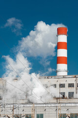 Obraz premium Pollution of the environment, ecology and air. Withdrawal of combustion products of soot, smoke and gases from the pipe of an industrial plant into the atmosphere against the background of a blue sky