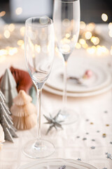 Xmas table settings in white and pink colors with trendy paper christmas trees on background, empty plates and glasses ready for festive dinner and party