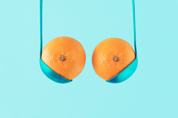 Breast and bra made with oranges or tangerines and blue ladles on isolated pastel blue background. Citrus fruits and kitchen equipment. Minimal aesthetic abstract idea of boobs. Creative food concept.
