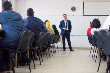 Male teacher or professor is giving interesting economy  lecture for students during lesson in the modern classroom