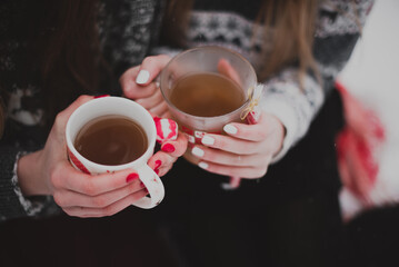 Close up fashion portrait of two sisters hugs and having fun, drinking tea winter time,wearing red santa hats and sweater,best friends couple outdoors, snowy weather
