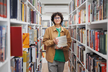 young beautiful woman with curly hair in the library among the shelves with books. a female student...