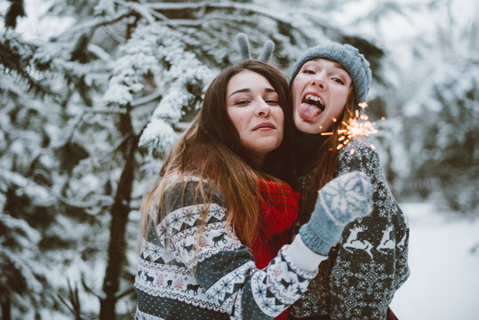 .Close up fashion portrait of two sisters hugs and having fun, holding sparklers in winter time forest, wearing sweaters and scarfs,best friends couple outdoors, snowy weather