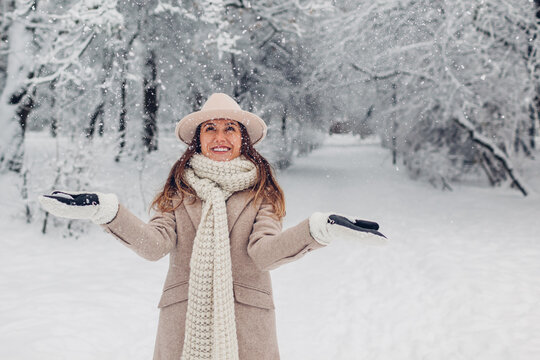 Happy Fashionable Young Woman Tossing Snow Up In Frosty Winter Park Wearing Stylish Warm Clothes And Having Fun.