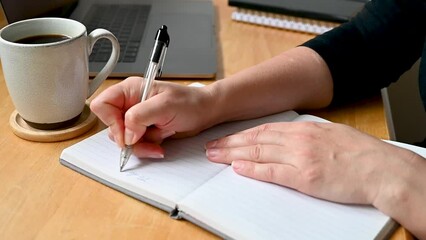 Close-up of woman hand writing To do list on notebook on table. Planning, working from home, education, goals. Selective focus.