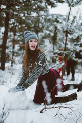 young teenage hipster girl having fun, make snowman in winter time forest, wearing sweaters and scarfs, outdoors, snowy weather