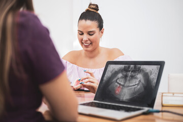 A dentist shows a patient some transparent splints for her treatment, in the PC an x-ray with an impacted tooth is seen, included.Mouth care.