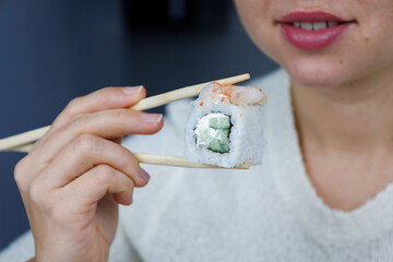 Japanese roll Philadelphia. The girl is holding sushi with chopsticks. Blurred background