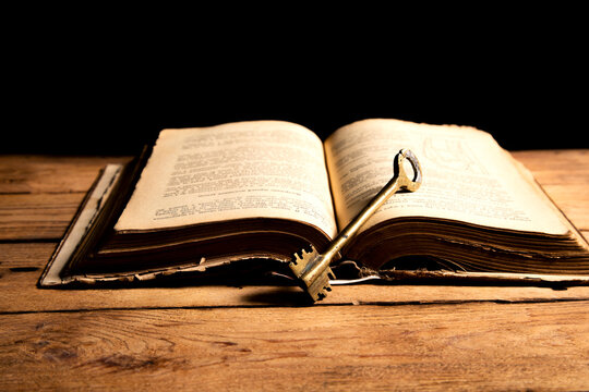 opened book and key on wooden background