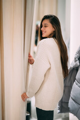 A girl trying on a white sweater in a store.