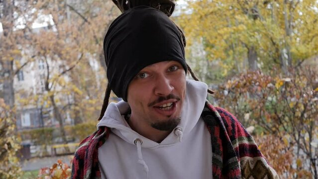 Young handsome man with dreadlocks and headband sings a subcultural song and claps his hands cheerfully dancing and smiling outdoors dressed in patterned plaid. capoeiro angola