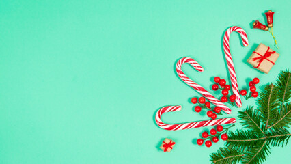 Obraz premium Candy canes and fir branches are decorated with red berries and small gift boxes. Turquoise background.
