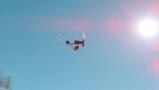 VOGEL, BOHINJ, JULIAN ALPS, SLOVENIA, MARCH 2022: SLOW MOTION: Male skier jumping big air kicker at snow park in snowy ski area. Extreme skier double rotating through the air and performing grab trick