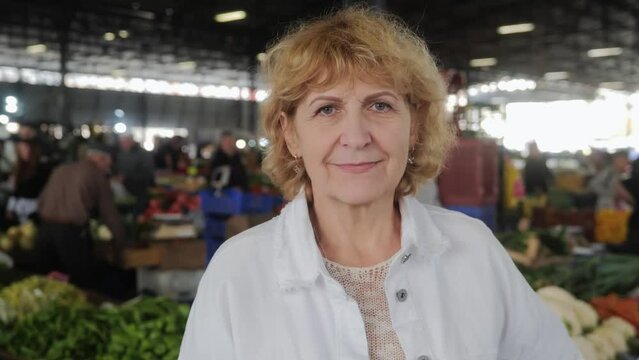 Portrait of an adult pretty woman with a smile looking at the camera, standing at the farmer's market. Buying healthy organic healthy products. Looks at the camera and smiles. High quality 4k footage