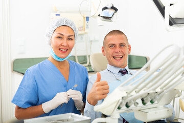 Satisfied european man smiling with white teeth showing thumbs up at dental clinic office