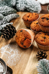 
muffins with chocolate on a wooden stand, powdered sugar, cones, Christmas tree branches nearby