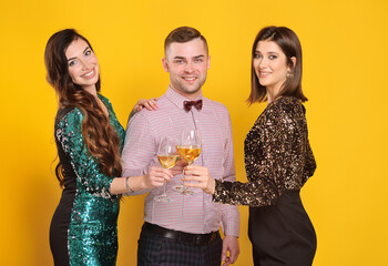 beautiful young women in cocktail dresses and an attractive young man are holding glasses of champagne and smiling