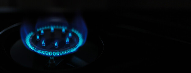 Natural gas blue fire flame on kitchen burner gas stove on dark background. Circular gas-jet. Flame...
