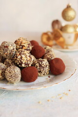 Chocolate truffles coated in a sprinkling of walnuts and cocoa on a white plate with a gold stripe, decorated with a gold bow on a white background, a warm Christmas atmosphere, xmas decorations.