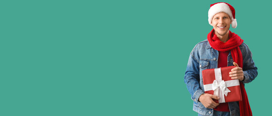 Happy man in Santa hat holding Christmas present on green background with space for text
