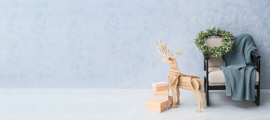 Wooden reindeer, Christmas gifts, armchair with plaid and mistletoe wreath near light wall with space for text