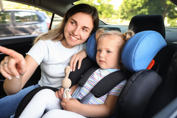 Fototapeta na wymiar Mother and her little daughter with toy buckled in car safety seat