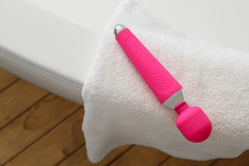 Pink vibrator and towel on bathtub in room, closeup
