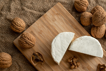 Composition of a cut cheese head with white and green mold and walnuts on a bamboo board on a background of burlap