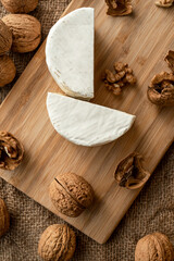 Composition of a cut cheese head with white and green mold and walnuts on a bamboo board on a background of burlap