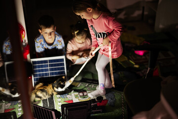 Children playing at home during a blackout using alternative lighting with solar panel.