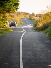 Small twisted asphalt road in a country side with a car parked off road. Selective focus. Travel and tourism concept.