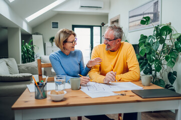 Senior couple sitting at table and looking into blueprints of their new home
