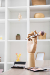 Wooden hand with makeup brush and eyeshadows on table in room, closeup