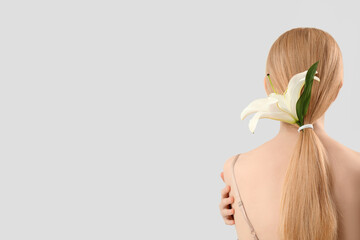 Blonde woman with ponytail and lily flower on light background - obrazy, fototapety, plakaty