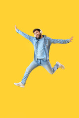 Obraz na płótnie Canvas Handsome bearded man in headphones jumping on yellow background
