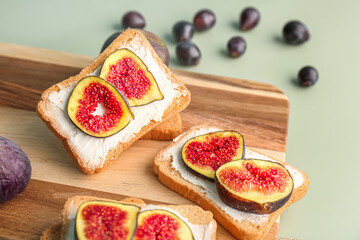 Wooden board of tasty bruschettas with cream cheese and ripe figs on color background, closeup