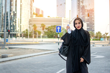 Fototapeta na wymiar Beautiful Arab woman in abaya holding water bottle and sport's bag on her way to a gym.