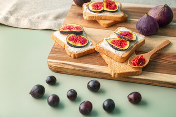 Wooden board of tasty bruschettas with cream cheese, figs and grapes on color background, closeup