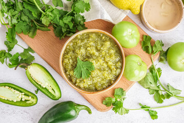 Composition with bowl of tasty green salsa sauce and ingredients on light background