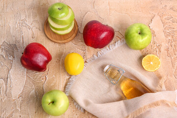 Bottle of apple cider vinegar wrapped in napkin and fruits on color background