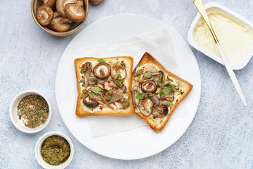 Plate of tasty toasts with cream cheese, mushrooms and pesto sauce on light table